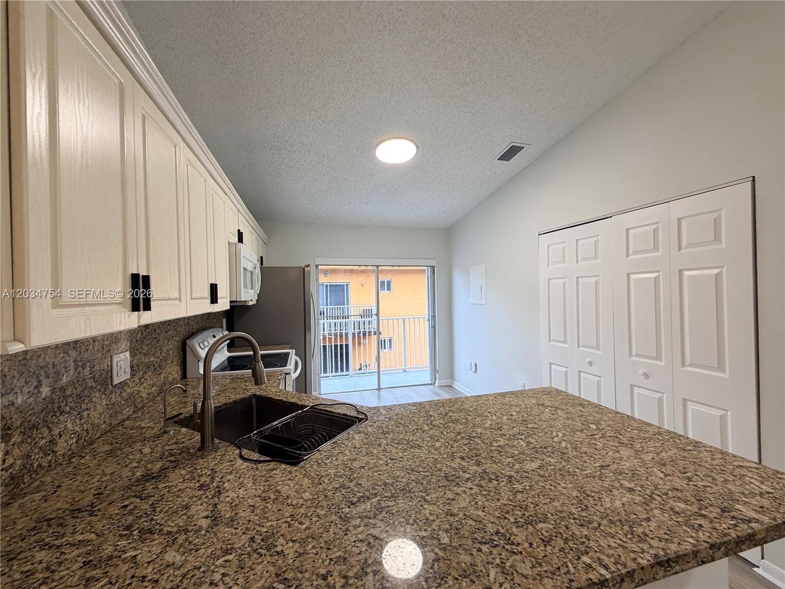 A kitchen features granite countertops, white cabinets, and a sliding glass door to a balcony — 7730 W 34th Ln # 202, Hialeah FL 33018, HIALEAH, FL