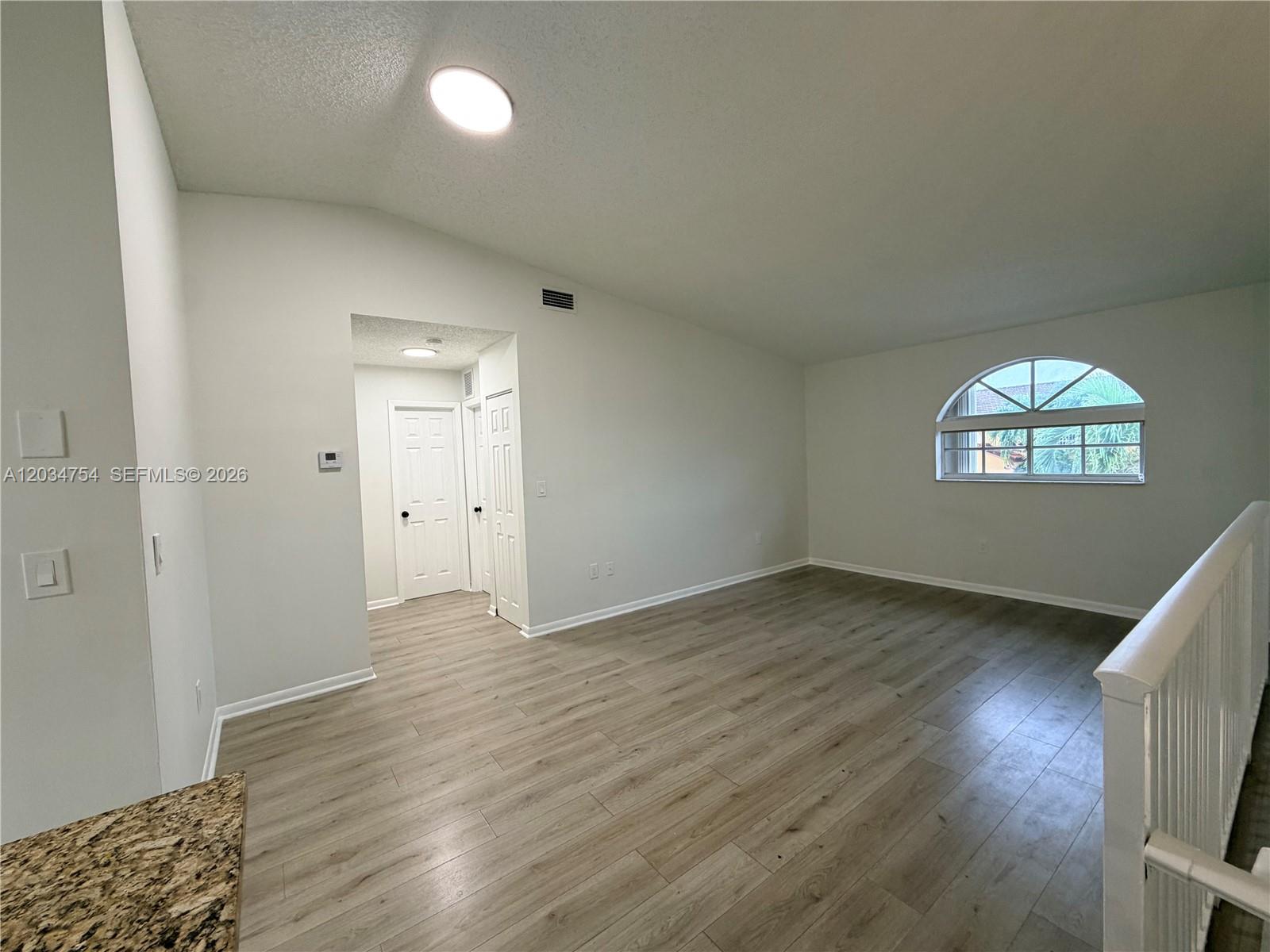 An empty room features light wood-look flooring, white walls, and an arched window — 7730 W 34th Ln # 202, Hialeah FL 33018, HIALEAH, FL