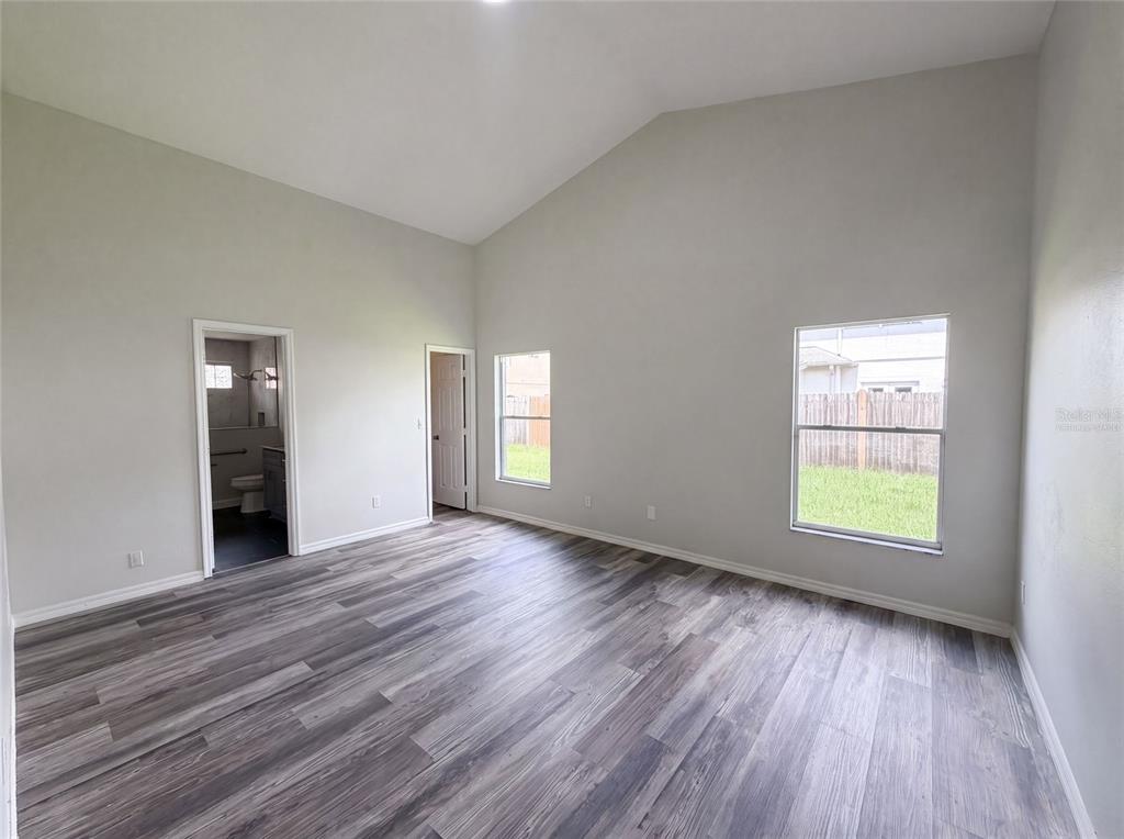An empty room with vaulted ceilings, gray wood-look flooring, two windows, and two doorways — 721 SUNBURST COVE LANE, WINTER GARDEN, FL
