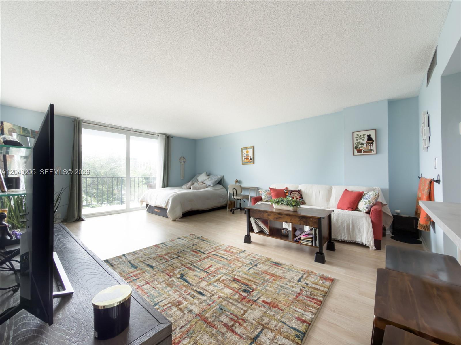 A studio apartment features a bed, sofa, coffee table, and a balcony with a railing — 12500 NE 15th Ave # 312, North Miami FL 33161, NORTH MIAMI, FL