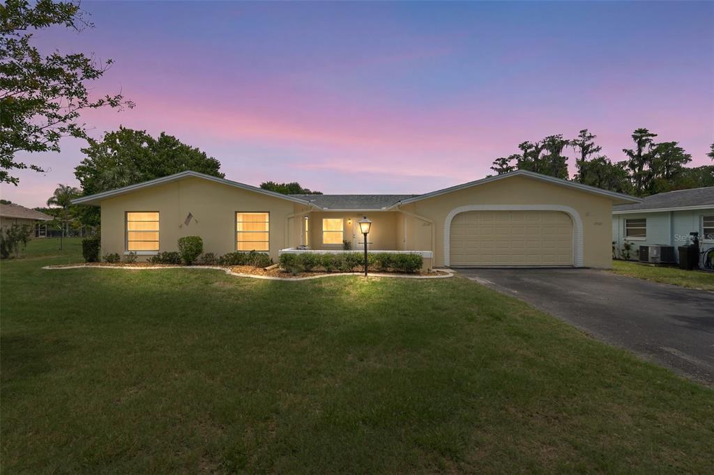 A single-story house with a yellow exterior, a two-car garage, and a front lawn — 12102 BOYNTON LANE UNIT B, NEW PORT RICHEY, FL
