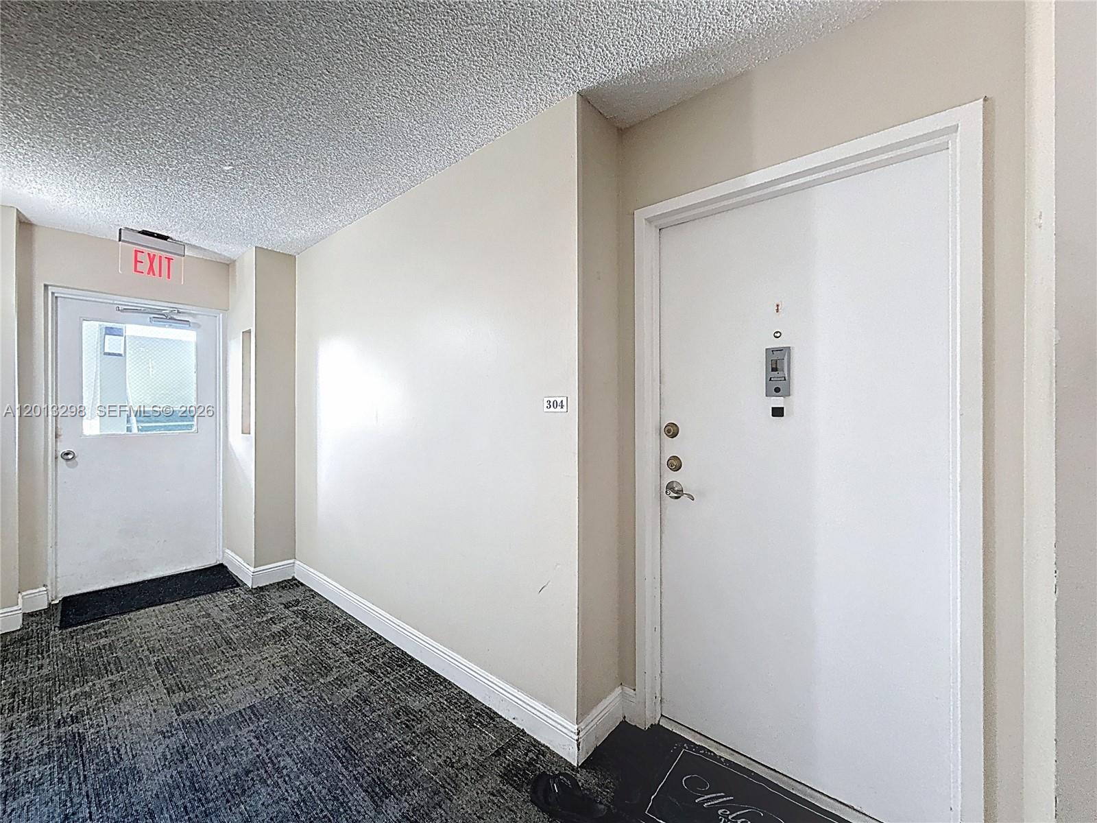 A hallway features a white door labeled 304, a textured ceiling, and an exit door — 2751 Taft St # 304, Hollywood FL 33020, HOLLYWOOD, FL
