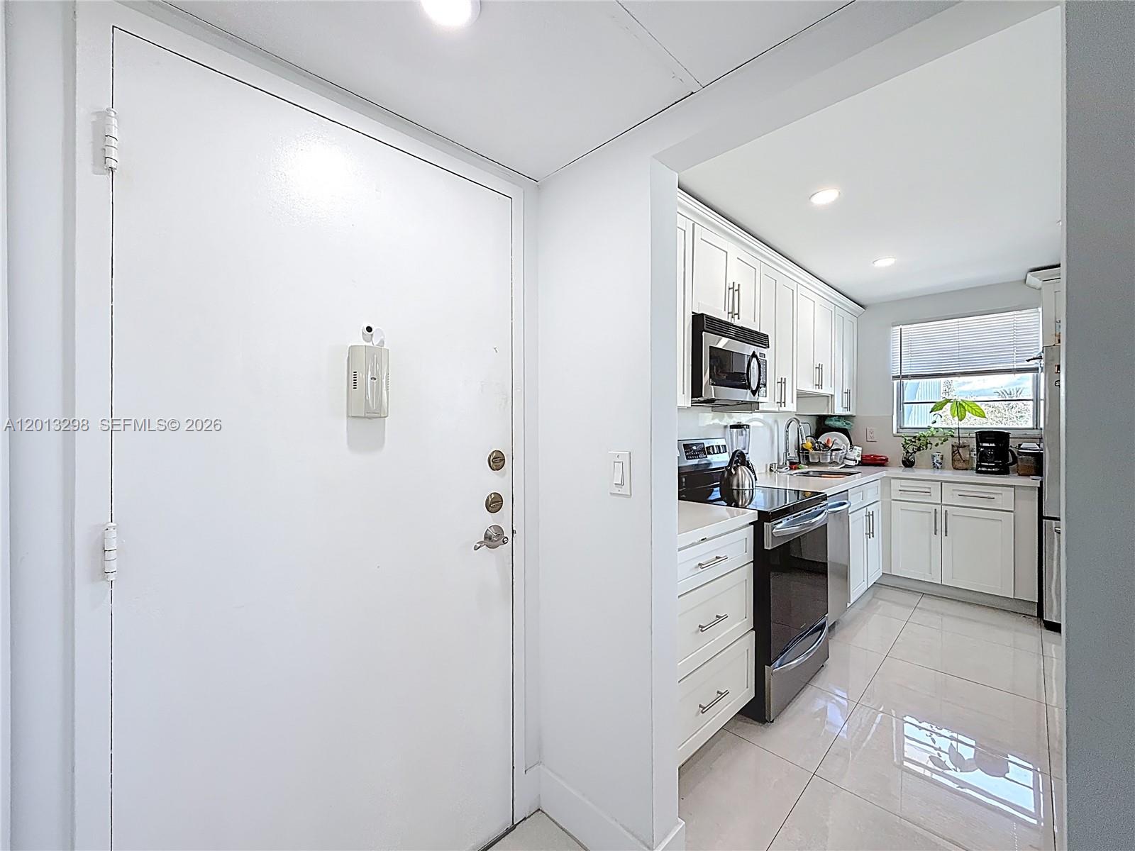 A white door opens into a kitchen featuring white cabinets, stainless steel appliances, and tile flooring — 2751 Taft St # 304, Hollywood FL 33020, HOLLYWOOD, FL