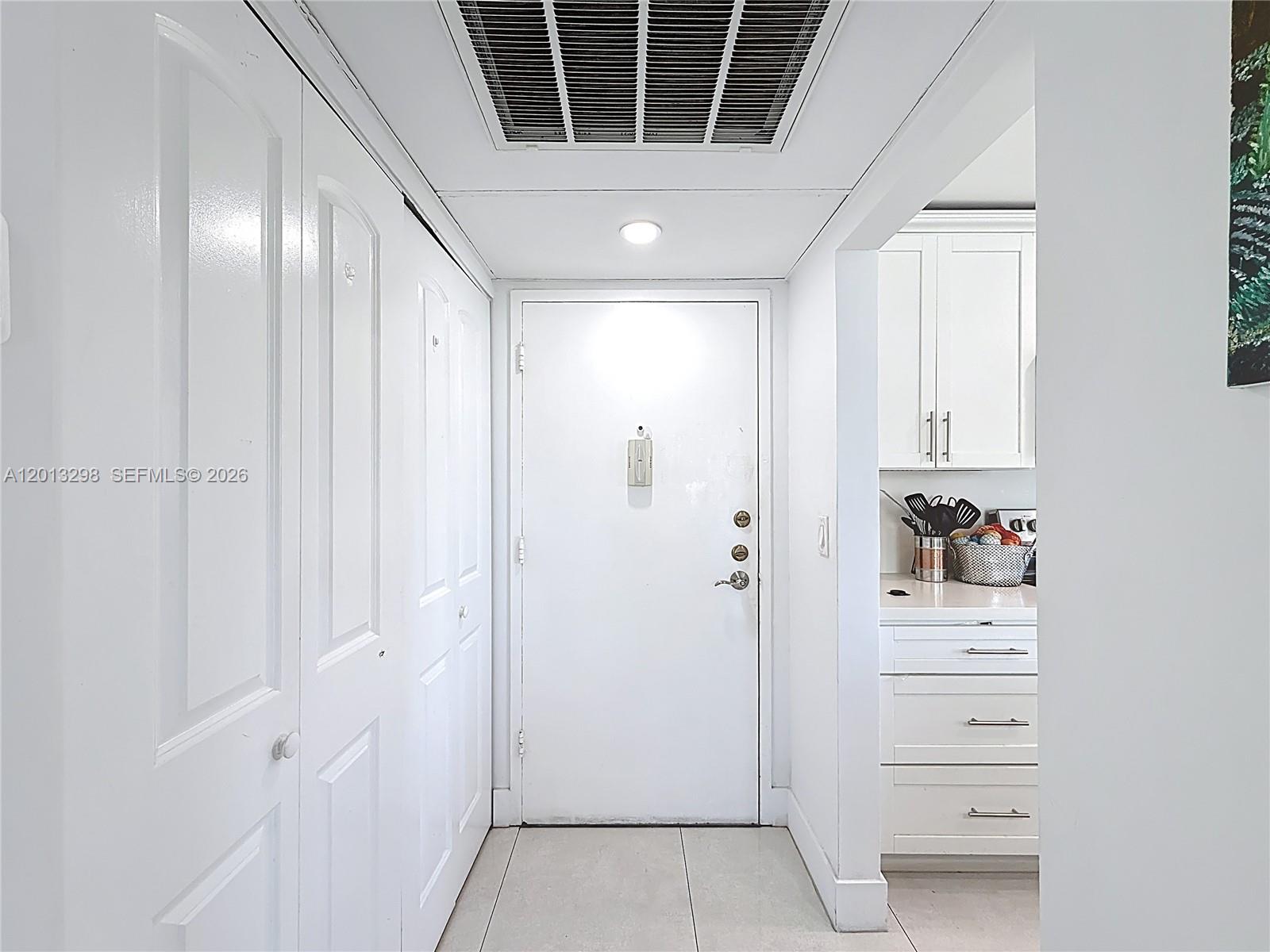 A white hallway features a central door, closet doors on the left, and kitchen cabinetry — 2751 Taft St # 304, Hollywood FL 33020, HOLLYWOOD, FL
