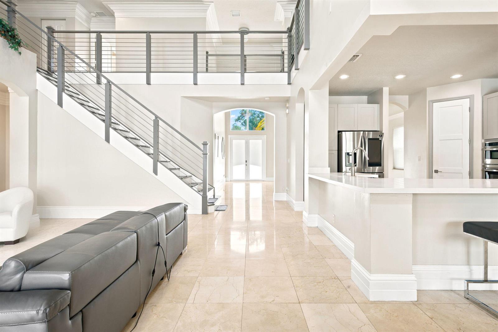 A modern living area features a staircase with metal railings, tile flooring, and a kitchen — 3766 W Gardenia Avenue, Weston FL 33332, WESTON, FL