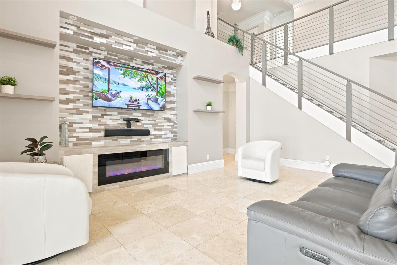 A living room features a tiled fireplace wall with a mounted television and a staircase — 3766 W Gardenia Avenue, Weston FL 33332, WESTON, FL