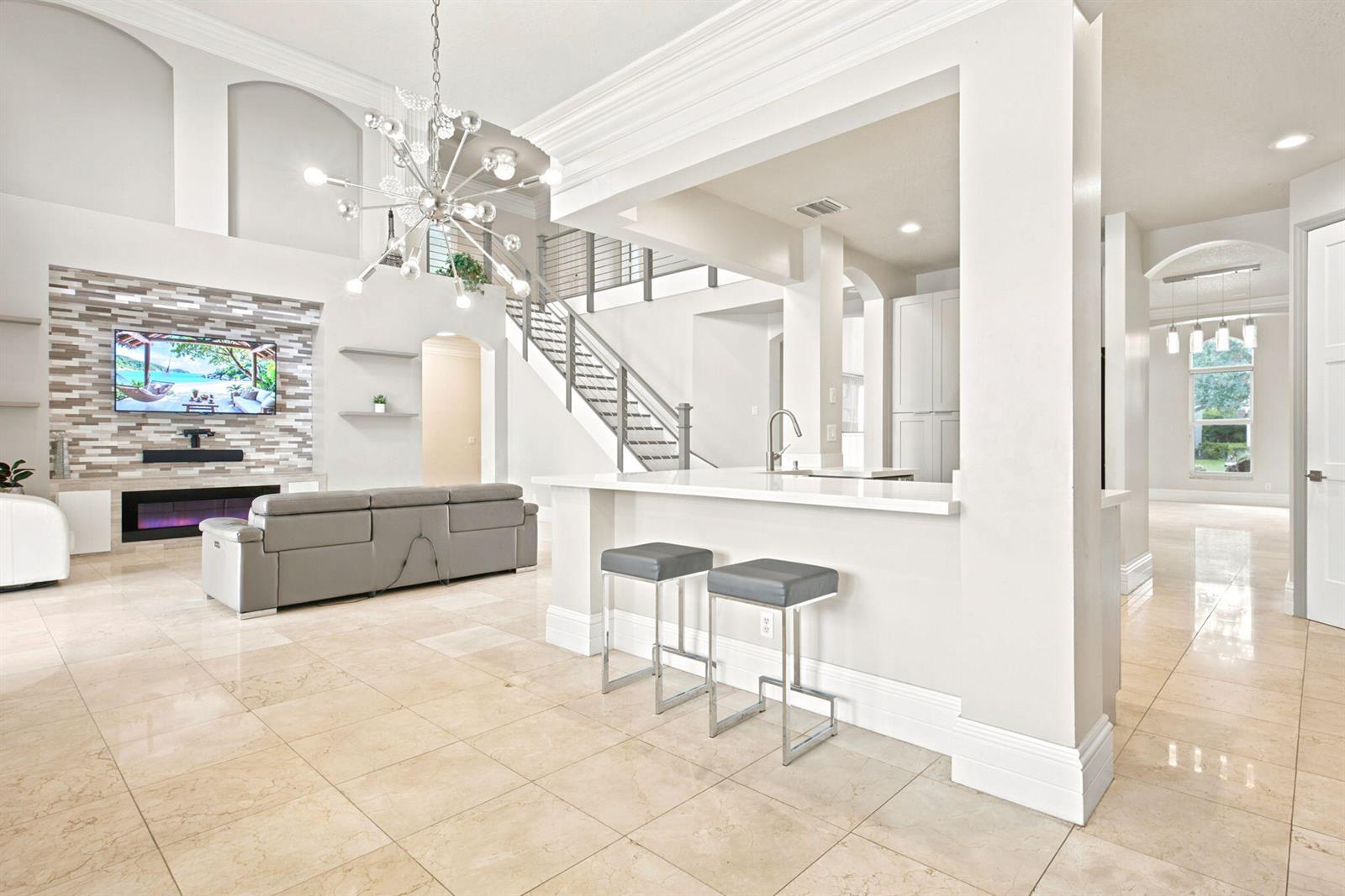 A modern living room features a stone fireplace wall, a staircase, and a kitchen bar — 3766 W Gardenia Avenue, Weston FL 33332, WESTON, FL