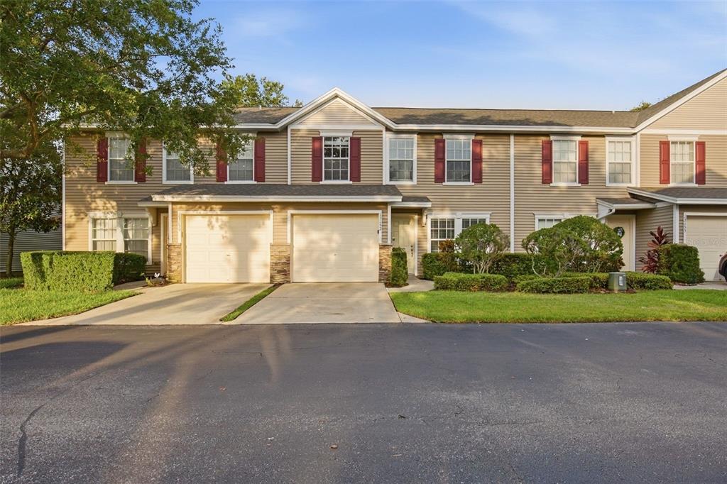 A tan, two-story townhouse with a two-car garage and red shutters under a clear sky — 13157 THOROUGHBRED LOOP, LARGO, FL