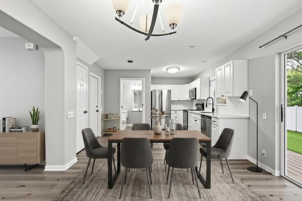 A dining area with a wooden table and grey chairs sits adjacent to a white kitchen — 13157 THOROUGHBRED LOOP, LARGO, FL