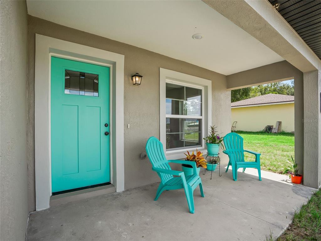 A covered front porch features a teal door, two matching chairs, and a small plant stand — 503 NW 60 AVENUE, OCALA, FL