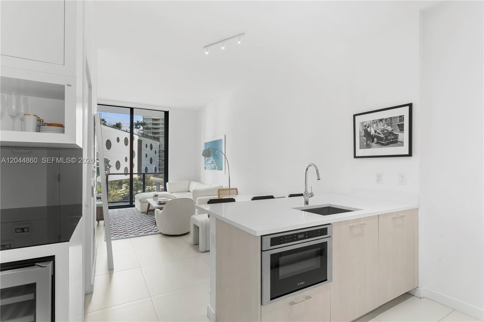 A modern kitchen with light wood cabinets and a white countertop overlooks a living area — 501 NE 31st St # 204, Miami FL 33137, MIAMI, FL