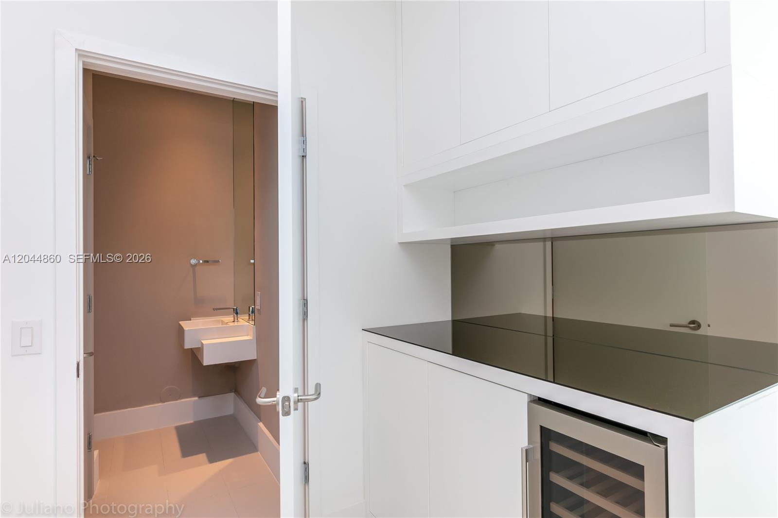 A modern wet bar with a wine cooler sits beside a doorway to a powder room — 501 NE 31st St # 204, Miami FL 33137, MIAMI, FL