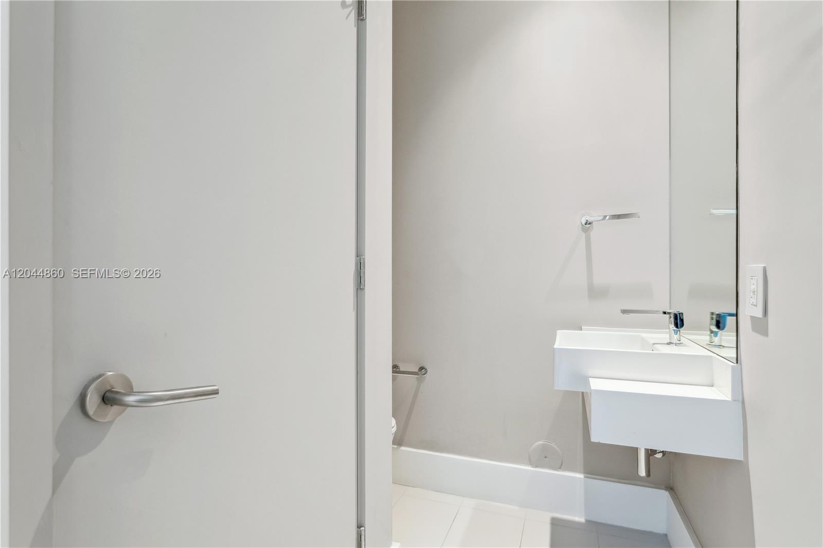 A minimalist powder room features a wall-mounted white sink, a mirror, and a toilet — 501 NE 31st St # 204, Miami FL 33137, MIAMI, FL