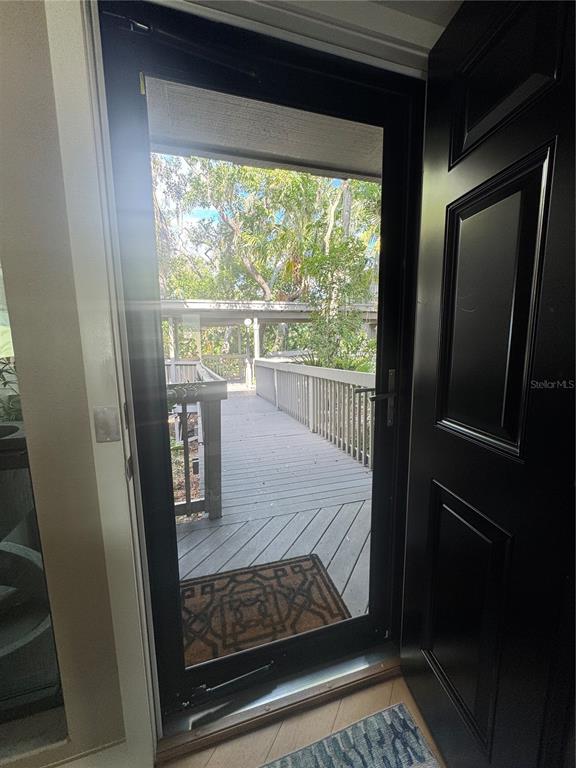 An open black door reveals a wooden deck and a walkway surrounded by trees — 1323 LANDINGS DRIVE UNIT 12, SARASOTA, FL