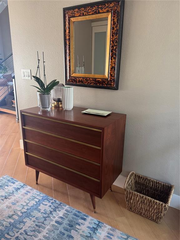A mid-century modern wooden dresser with brass accents sits below a tortoiseshell-framed mirror — 1323 LANDINGS DRIVE UNIT 12, SARASOTA, FL