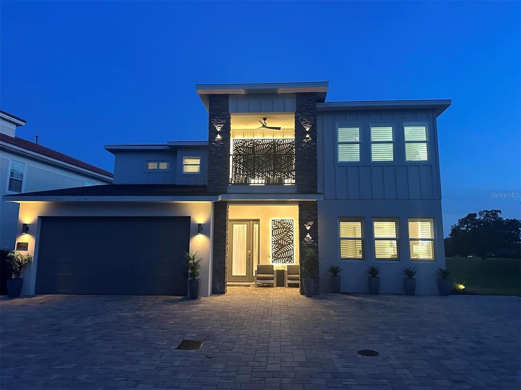 A two-story modern house with a stone-accented facade, a garage, and a balcony at dusk — 7442 GATHERING COURT, KISSIMMEE, FL