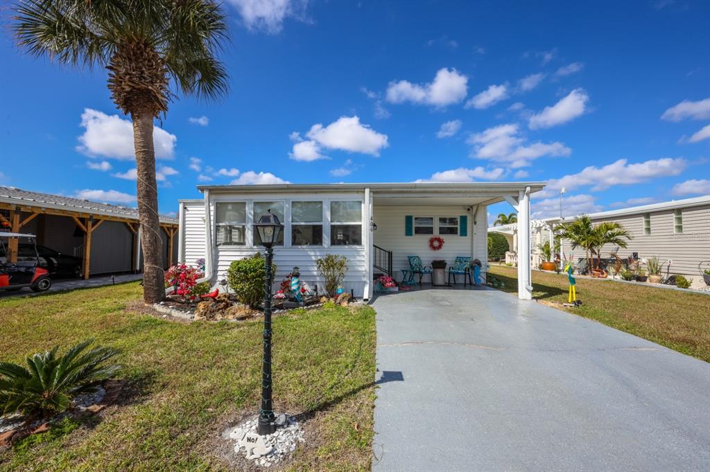 A white mobile home with a carport, blue front door, and a palm tree outside — 2100 KINGS HIGHWAY UNIT 406, PORT CHARLOTTE, FL