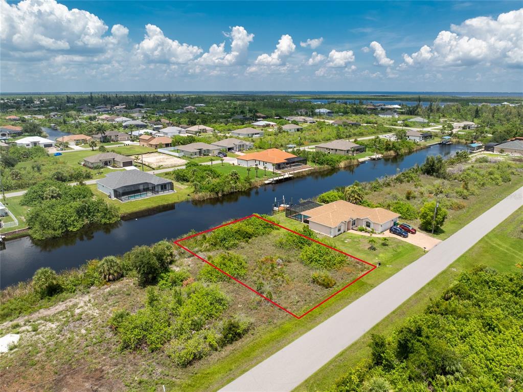An aerial view shows a vacant, rectangular waterfront lot outlined in red next to a house — 15610 APPLEWHITE CIRCLE, PORT CHARLOTTE, FL