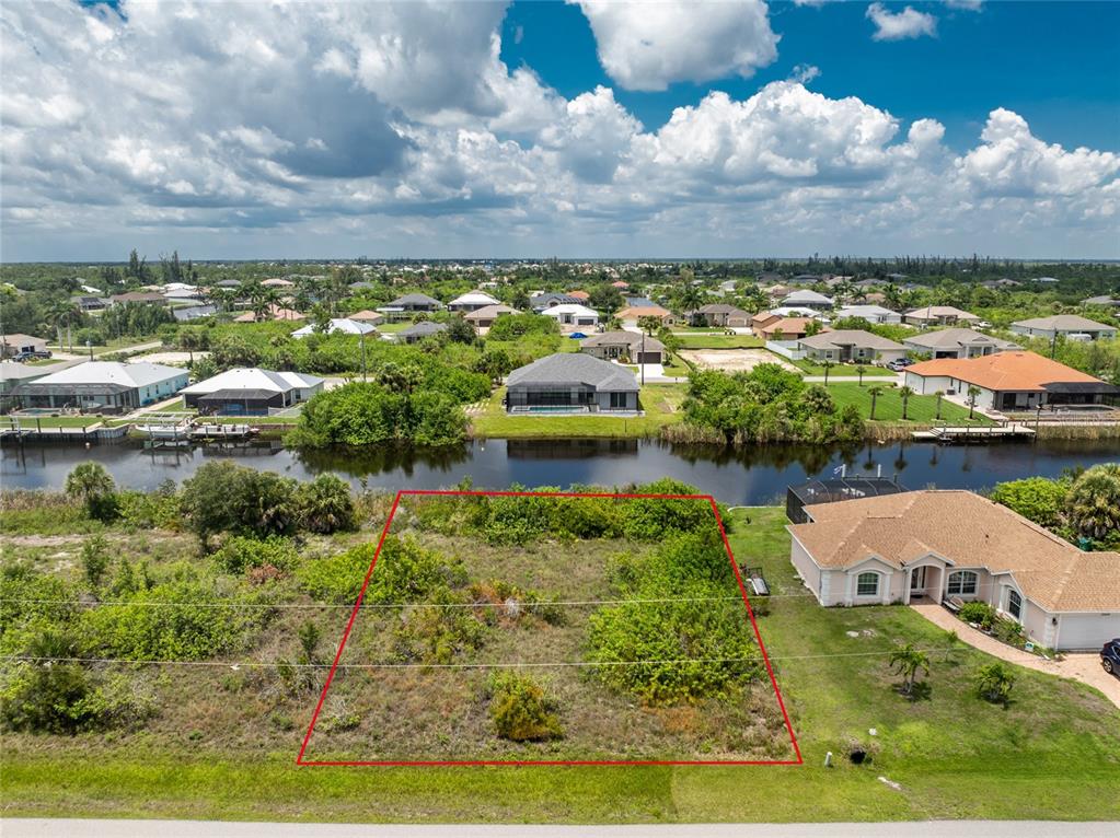 An aerial view shows a vacant, rectangular residential lot outlined in red beside a canal — 15610 APPLEWHITE CIRCLE, PORT CHARLOTTE, FL