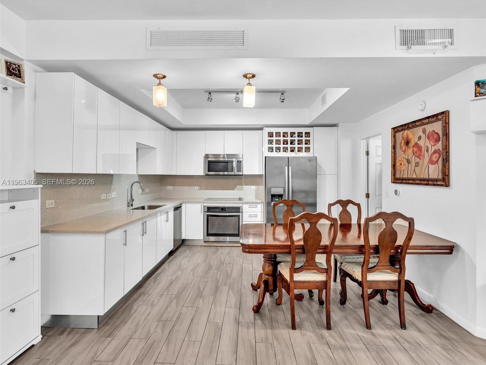 A modern kitchen features white cabinets, stainless steel appliances, and a wooden dining set — 999 SW 1st Ave # 1201, Miami FL 33130, MIAMI, FL