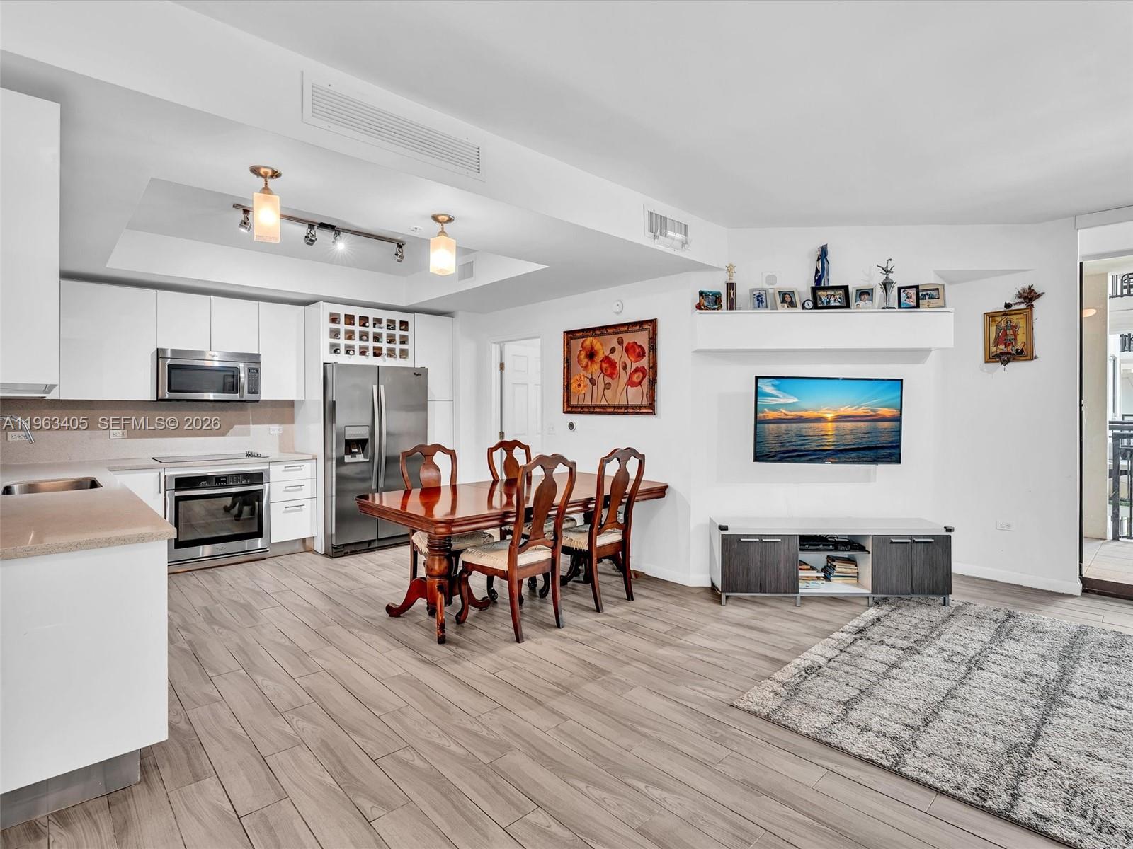 An open-concept kitchen and dining area features white cabinetry, stainless steel appliances, and wood flooring — 999 SW 1st Ave # 1201, Miami FL 33130, MIAMI, FL