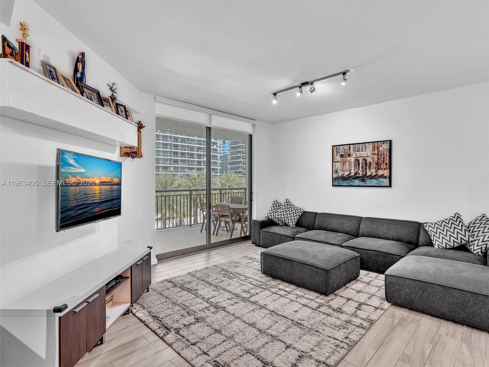 A modern living room features a grey sectional sofa, a television, and a balcony view — 999 SW 1st Ave # 1201, Miami FL 33130, MIAMI, FL