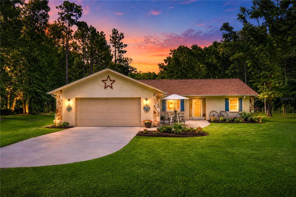 A single-story house with a two-car garage, stone accents, and a lawn at sunset — 15970 NW 53RD STREET, MORRISTON, FL