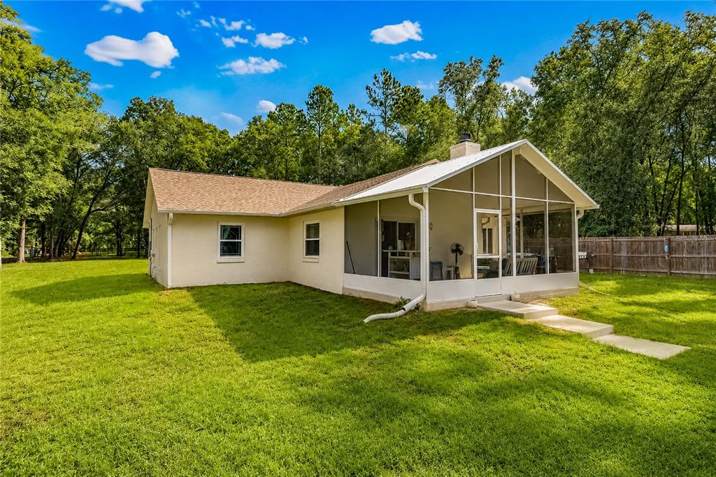 A beige house with a screened-in porch sits on a grassy lawn under blue skies — 15970 NW 53RD STREET, MORRISTON, FL