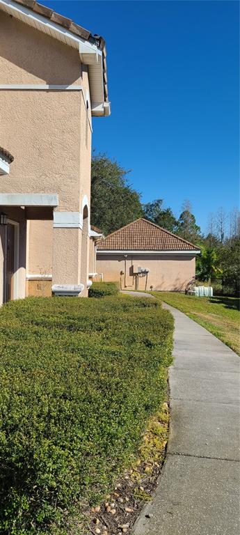 A concrete sidewalk runs alongside a beige stucco building and a hedge toward a garage — 17902 VILLA CREEK DRIVE UNIT 17902, TAMPA, FL
