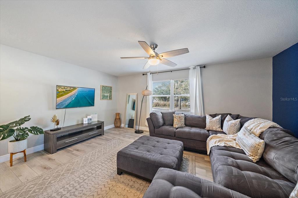 A living room features a grey sectional sofa, a television, and light wood-look flooring — 3710 IROQUOIS AVENUE, SARASOTA, FL