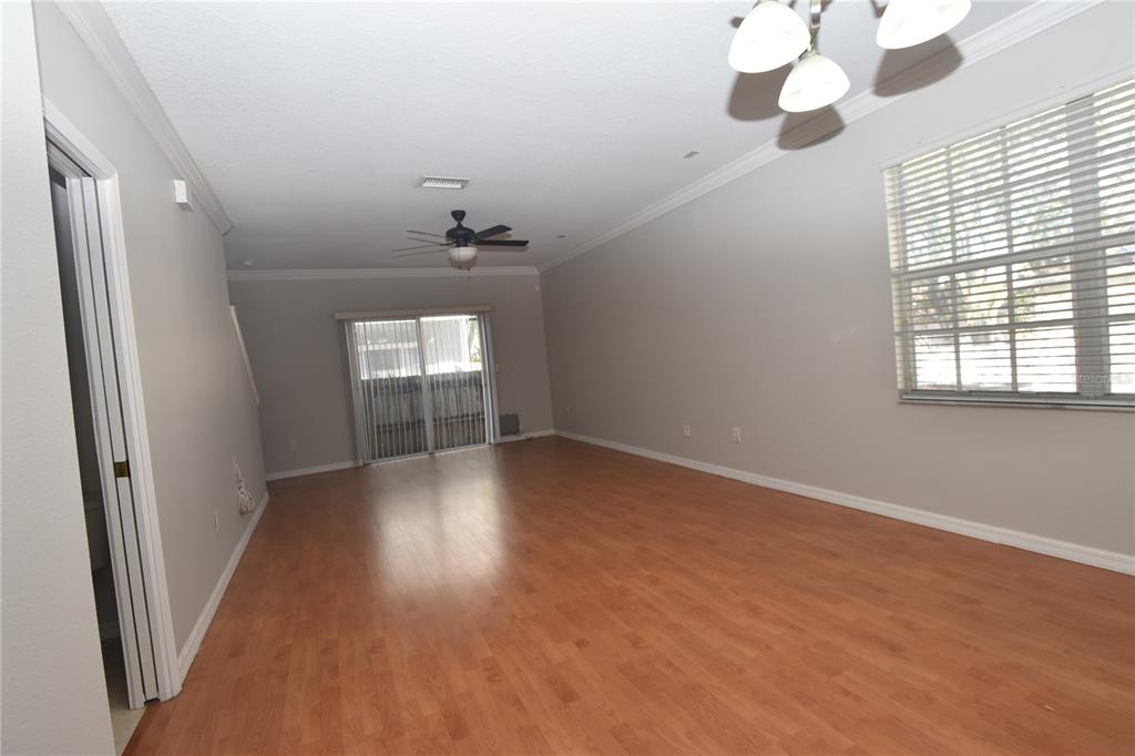An empty living room features light gray walls, wood-look flooring, a ceiling fan, and sliding doors — 4901 ELIZABETH ANNE CIRCLE, TAMPA, FL