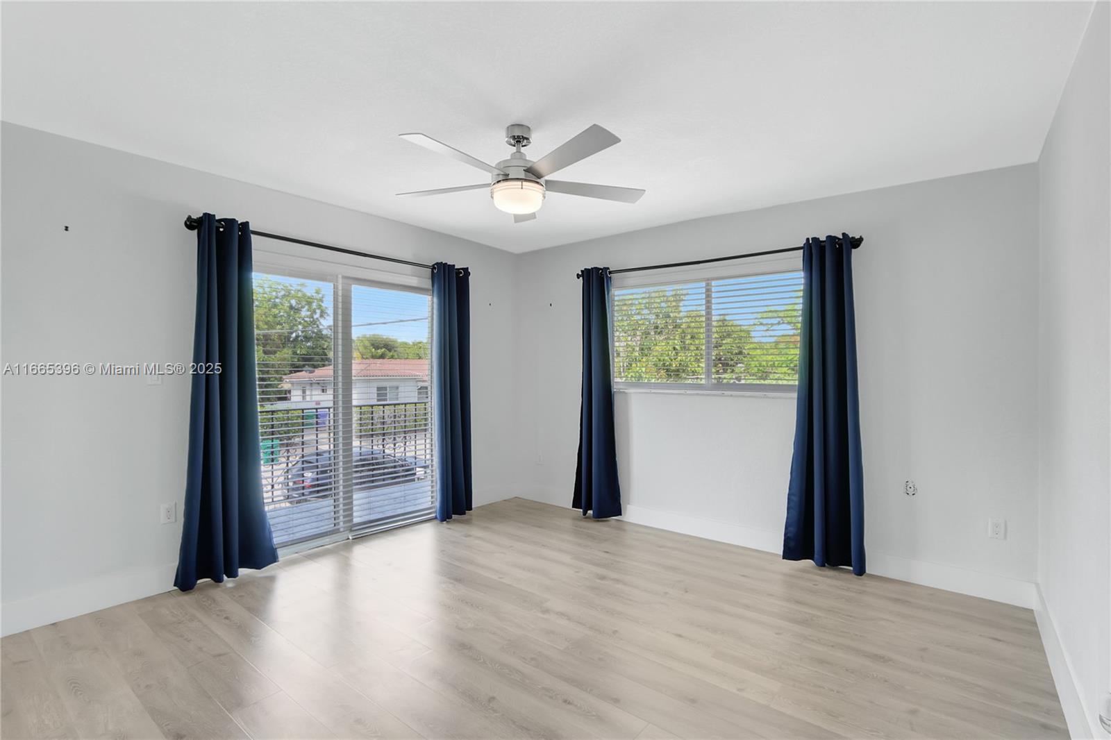 An empty bedroom features light wood flooring, a ceiling fan, and dark blue curtains — 1359 SW 11th St, Miami FL 33135, MIAMI, FL