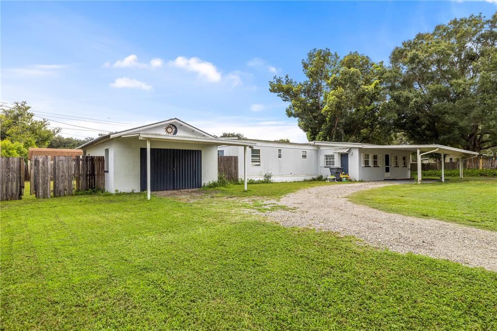 A single-story house with a gravel driveway, attached carport, and a wooden fence — 1733 OAKLAND ROAD W, LAKELAND, FL