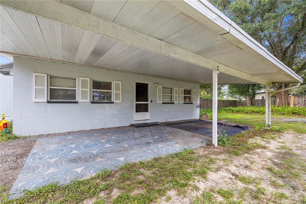 A light blue concrete block house features a large covered carport and a patterned patio — 1733 OAKLAND ROAD W, LAKELAND, FL