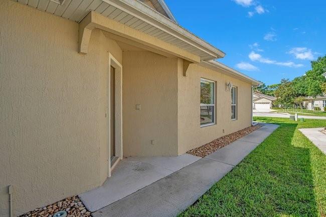A side view of a beige stucco house with a concrete walkway and green lawn — 208 LAMONTE POINT CT, DEBARY, FL