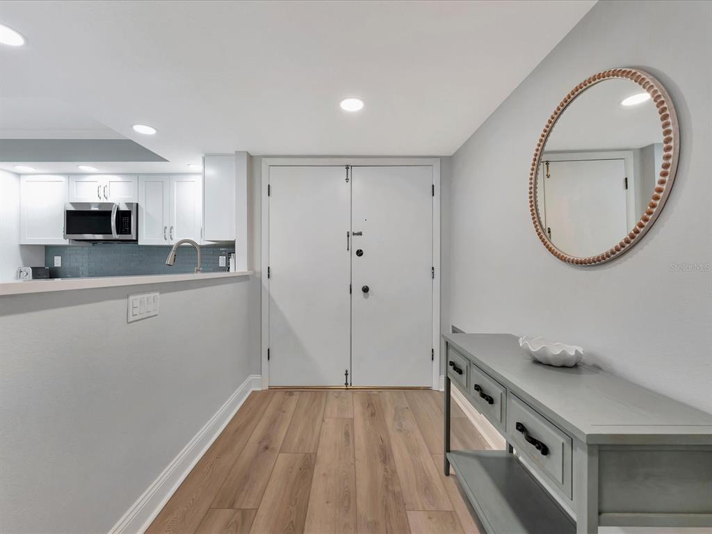 An entryway features light wood flooring, a gray console table, a round mirror, and double doors — 1430 GULF BOULEVARD UNIT 612, CLEARWATER BEACH, FL