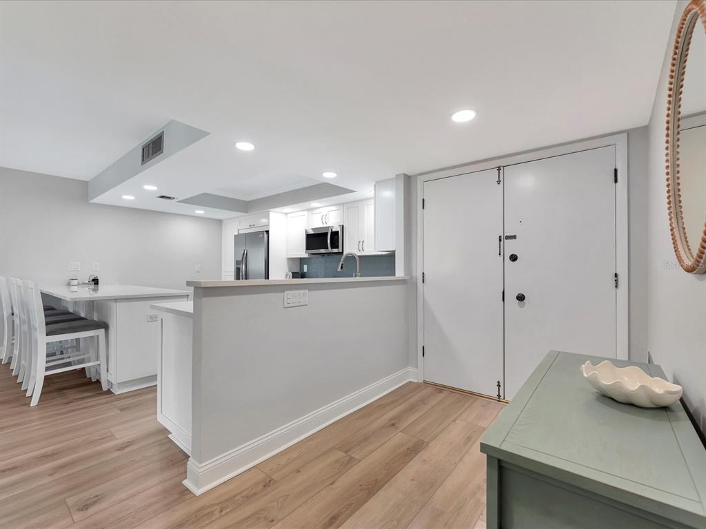 A kitchen with white cabinets and an island overlooks a room with light wood flooring — 1430 GULF BOULEVARD UNIT 612, CLEARWATER BEACH, FL