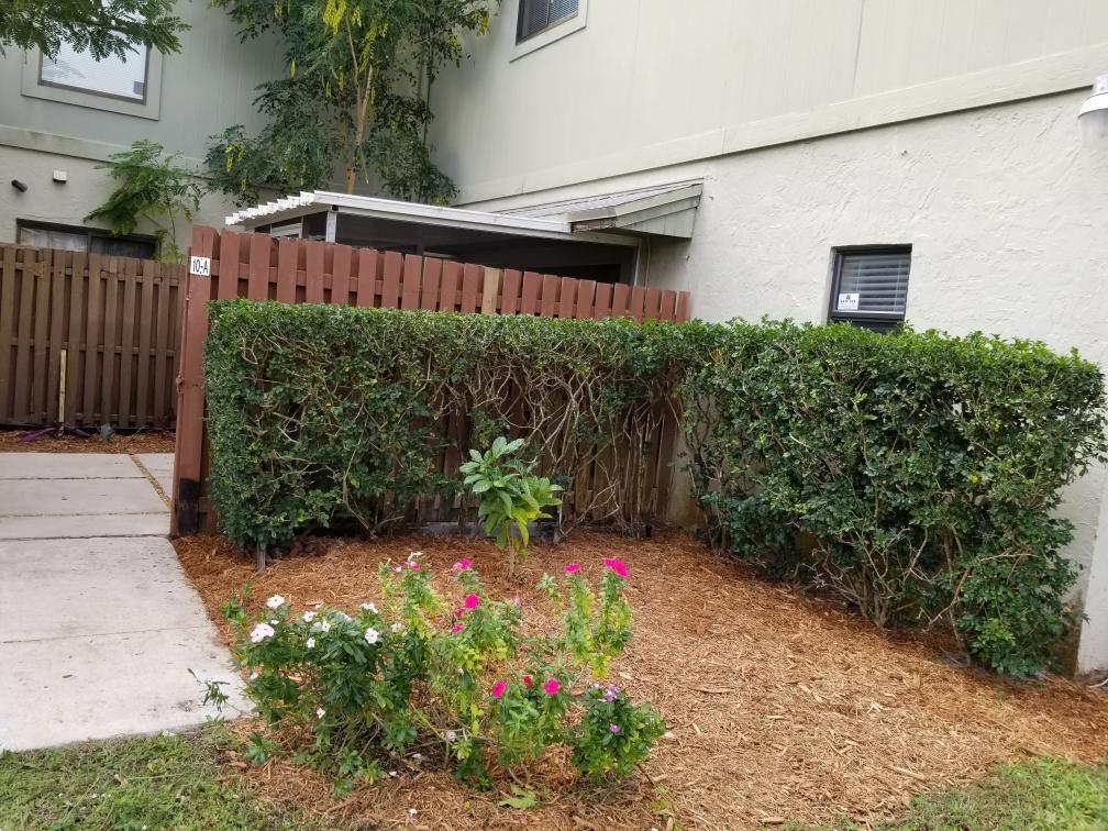 A small garden bed with flowers and mulch sits in front of a wooden fence — 10 Crossings Circle # A, Boynton Beach FL 33435, BOYNTON BEACH, FL