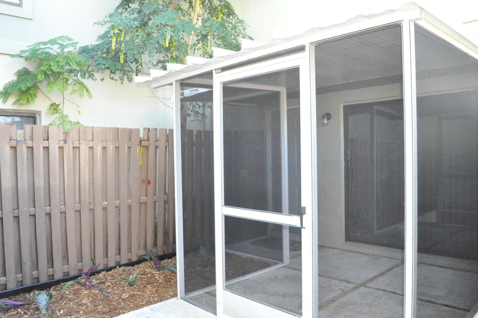 A screened-in patio with a concrete floor sits next to a wooden privacy fence — 10 Crossings Circle # A, Boynton Beach FL 33435, BOYNTON BEACH, FL