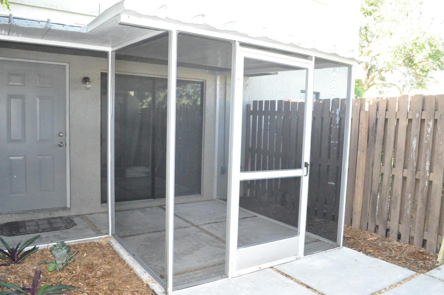 A screened-in patio with a concrete floor, a metal door, and a wooden privacy fence — 10 Crossings Circle # A, Boynton Beach FL 33435, BOYNTON BEACH, FL