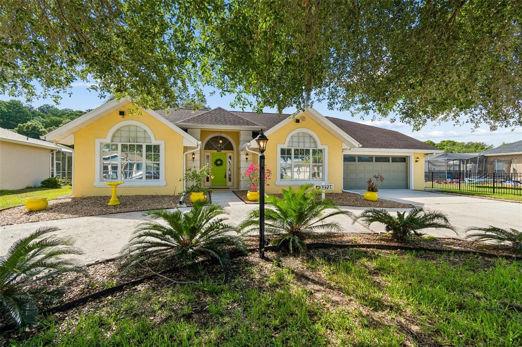 A yellow single-story house with a green front door, arched windows, and a concrete driveway — 12728 FLAMINGO PARKWAY, SPRING HILL, FL