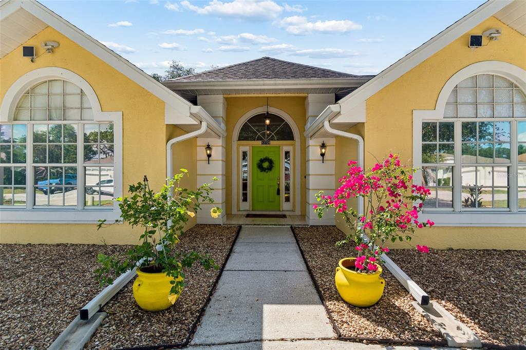 A yellow house exterior features a bright green front door, arched windows, and two potted plants — 12728 FLAMINGO PARKWAY, SPRING HILL, FL