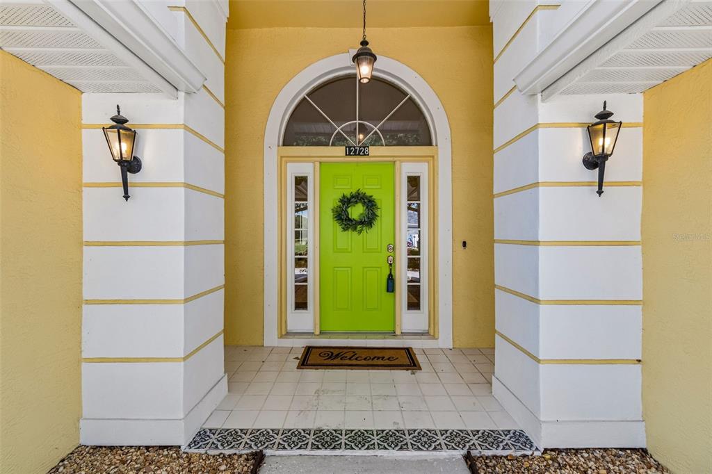A bright green front door with a wreath sits under an arched transom window — 12728 FLAMINGO PARKWAY, SPRING HILL, FL