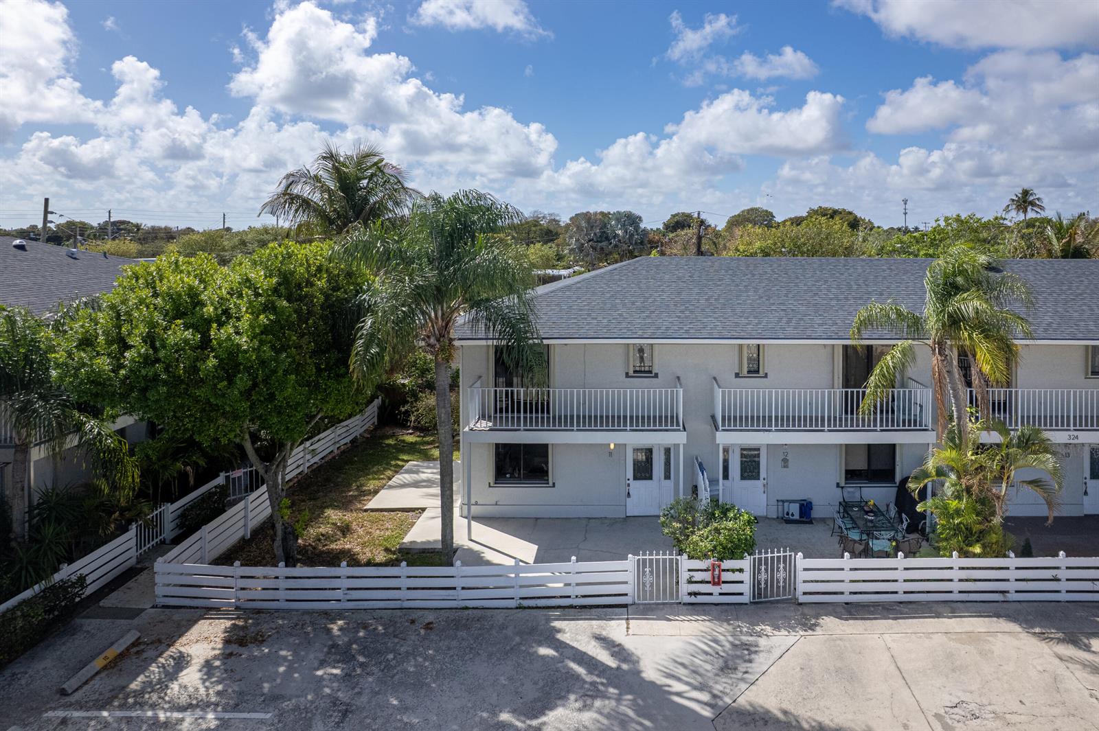 An exterior view of a two-story townhouse with a white fence and palm trees — 324 W Pine Street # 11, Lantana FL 33462, LANTANA, FL