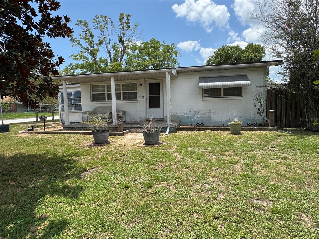 A single-story white house with a front porch and metal awning stands on a lawn — 1404 EMMETT STREET, KISSIMMEE, FL