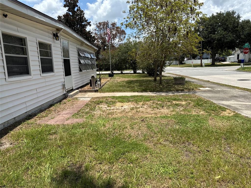 The exterior of a white, single-story house with a lawn, sidewalk, and street corner — 1404 EMMETT STREET, KISSIMMEE, FL