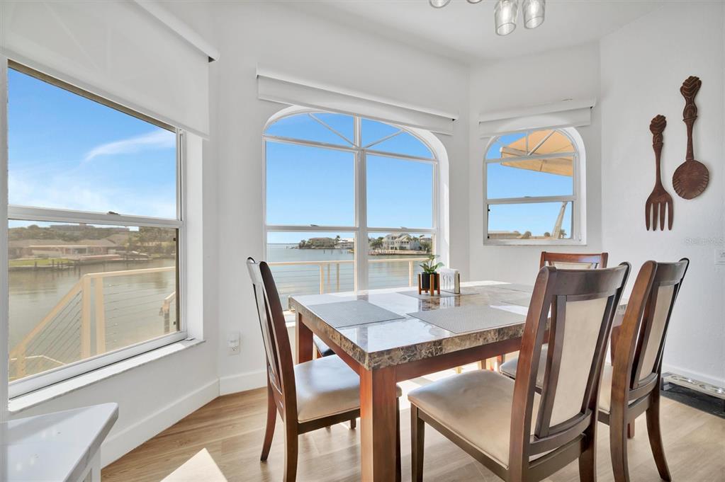 A dining area features a marble-topped table, wooden chairs, and large windows overlooking the water — 5918 SKIMMER POINT BOULEVARD S, GULFPORT, FL