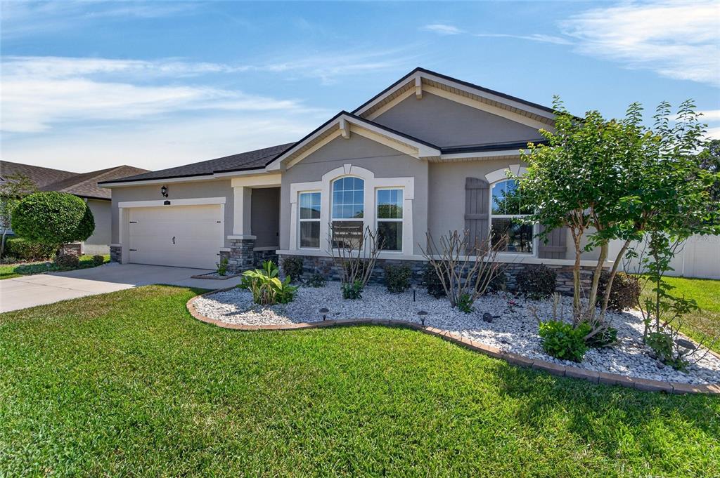 A single-story house with a beige stucco exterior, stone accents, and a front-facing garage — 13017 SATIN LILY DRIVE, RIVERVIEW, FL