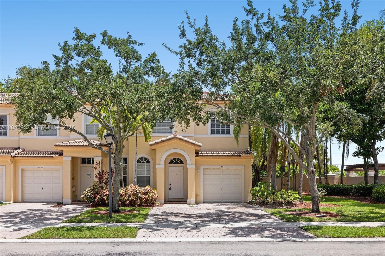 A two-story yellow stucco townhouse with a paved driveway and two garage doors — 8401 SW 25th Ct # 106, Miramar FL 33025, MIRAMAR, FL