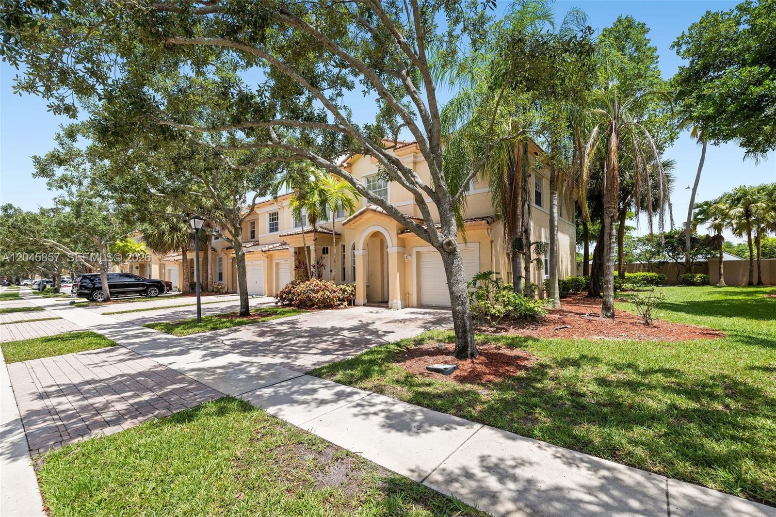 A two-story tan townhouse with a paved driveway and mature trees in the front yard — 8401 SW 25th Ct # 106, Miramar FL 33025, MIRAMAR, FL